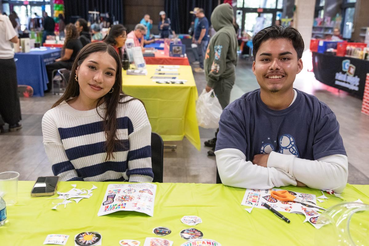 Two students looking at the camera. They are working the check in booth at the event