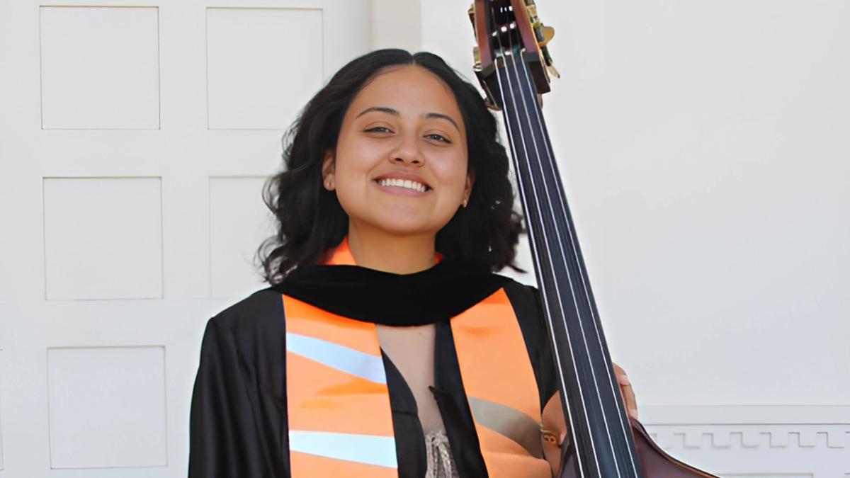 RCC alumni Angelina Salcedo in her orange and black regalia with her musical instrument- cello