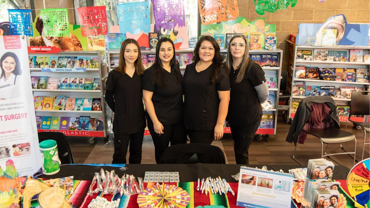 Four women dressed in black behind a colorful table, advertising the book fair