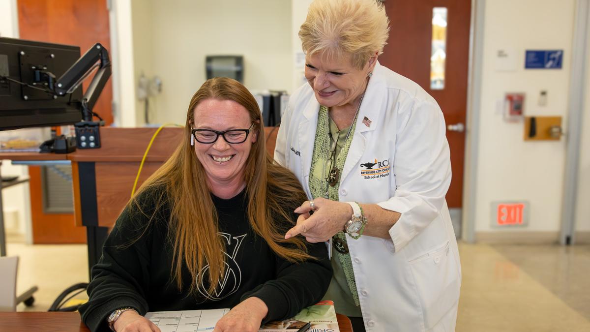 Nursing faculty assisting a student who is sitting at a table with a computer