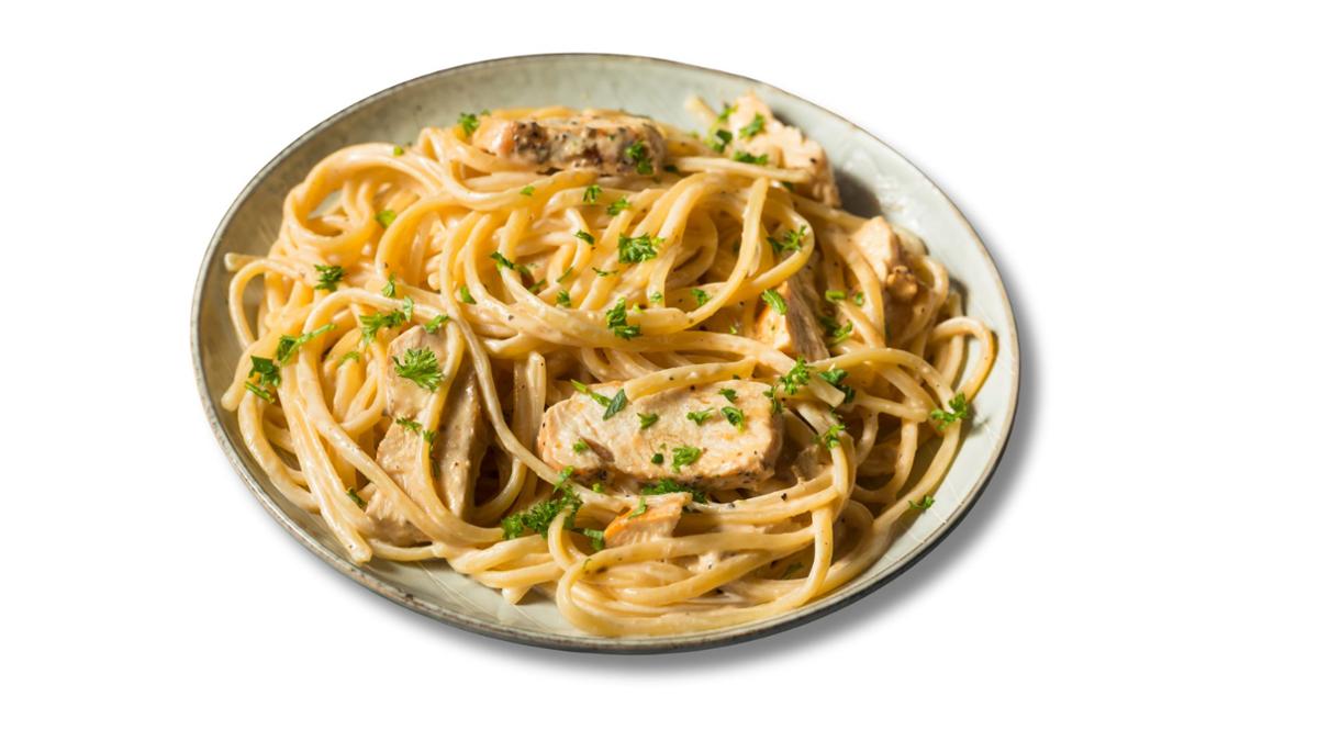 A plate of creamy chicken alfredo pasta with linguine noodles, sliced seasoned chicken, and parsley sprinkled on top.