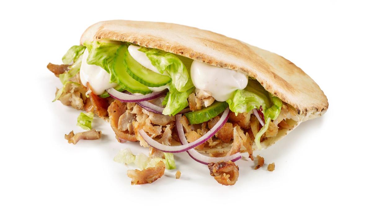 Special 1 Pita bread filled with sliced grilled meat, cucumber, red onion, lettuce, and creamy sauce, with some filling spilling out onto a white surface.
